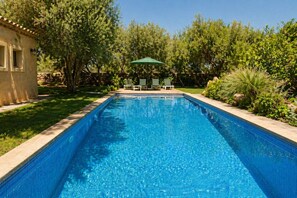 Una piscina rectangular con borde de azulejos, rodeada de césped y árboles.