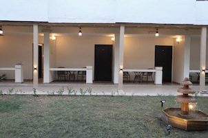 A covered outdoor area with tables and chairs, a black door, and a fountain.