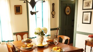 A dining room with a wooden table, chairs, and a chandelier. There are framed pictures on the wall and a clock. - Connecticut Colonial with River and Sunset Views! (East Haddam)