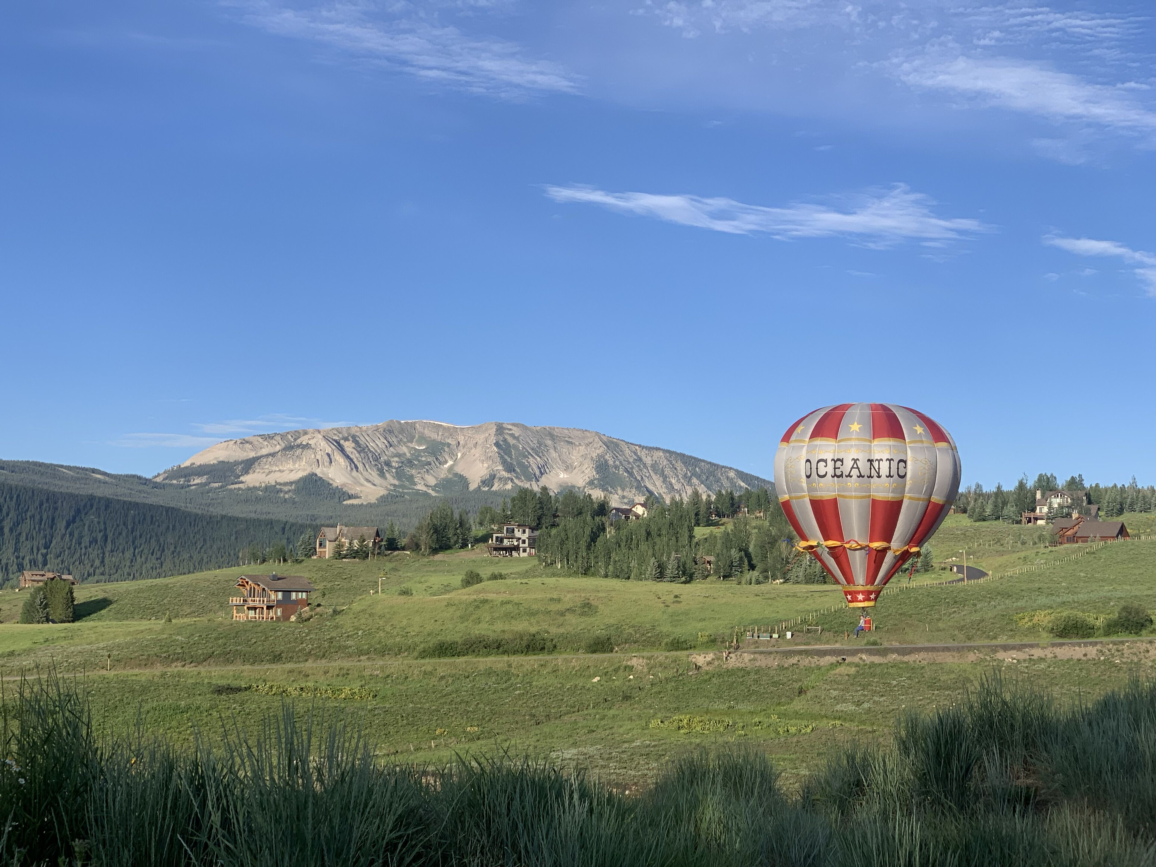 A hot air balloon with "OCEANIC" written on it, flying over a mountainous landscape with houses and greenery.