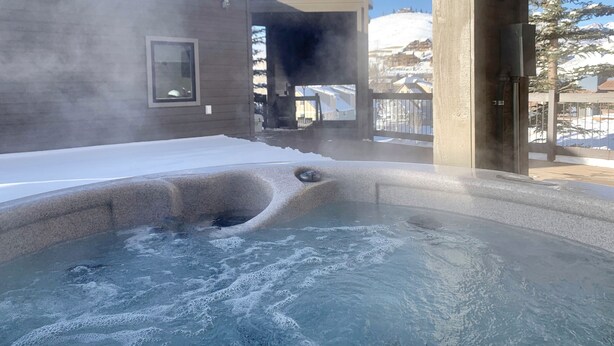 Een hottub met uitzicht op een besneeuwd landschap en een klok op een paal.