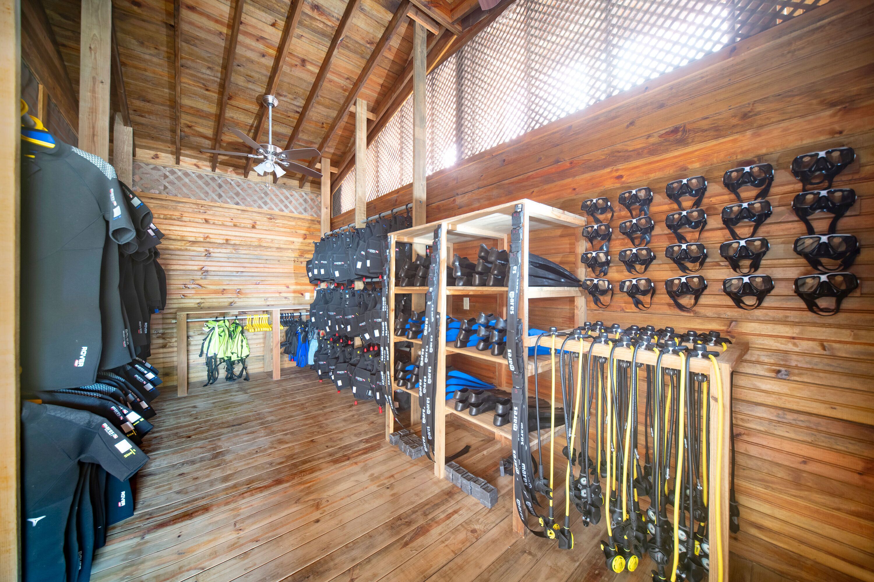 Una habitación con paredes y techo de madera, que exhibe filas de zapatos negros y azules en estantes y colgadores.