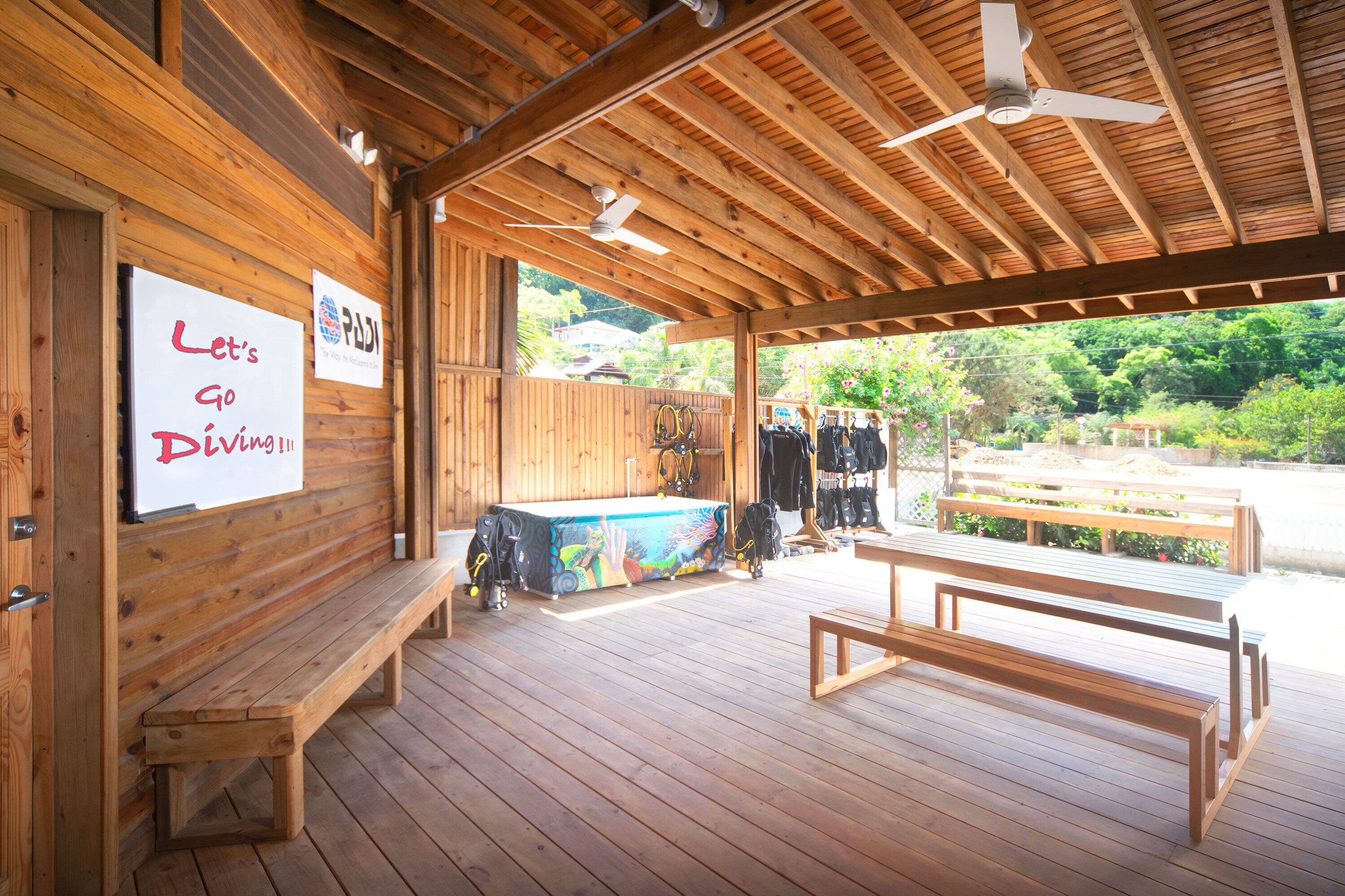 A wooden deck with benches and a pool table, a sign reading "Let's Go Diving!!!", and a view of greenery outside.