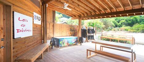 A wooden deck with benches and a pool table, a sign reading "Let's Go Diving!!!", and a view of greenery outside.