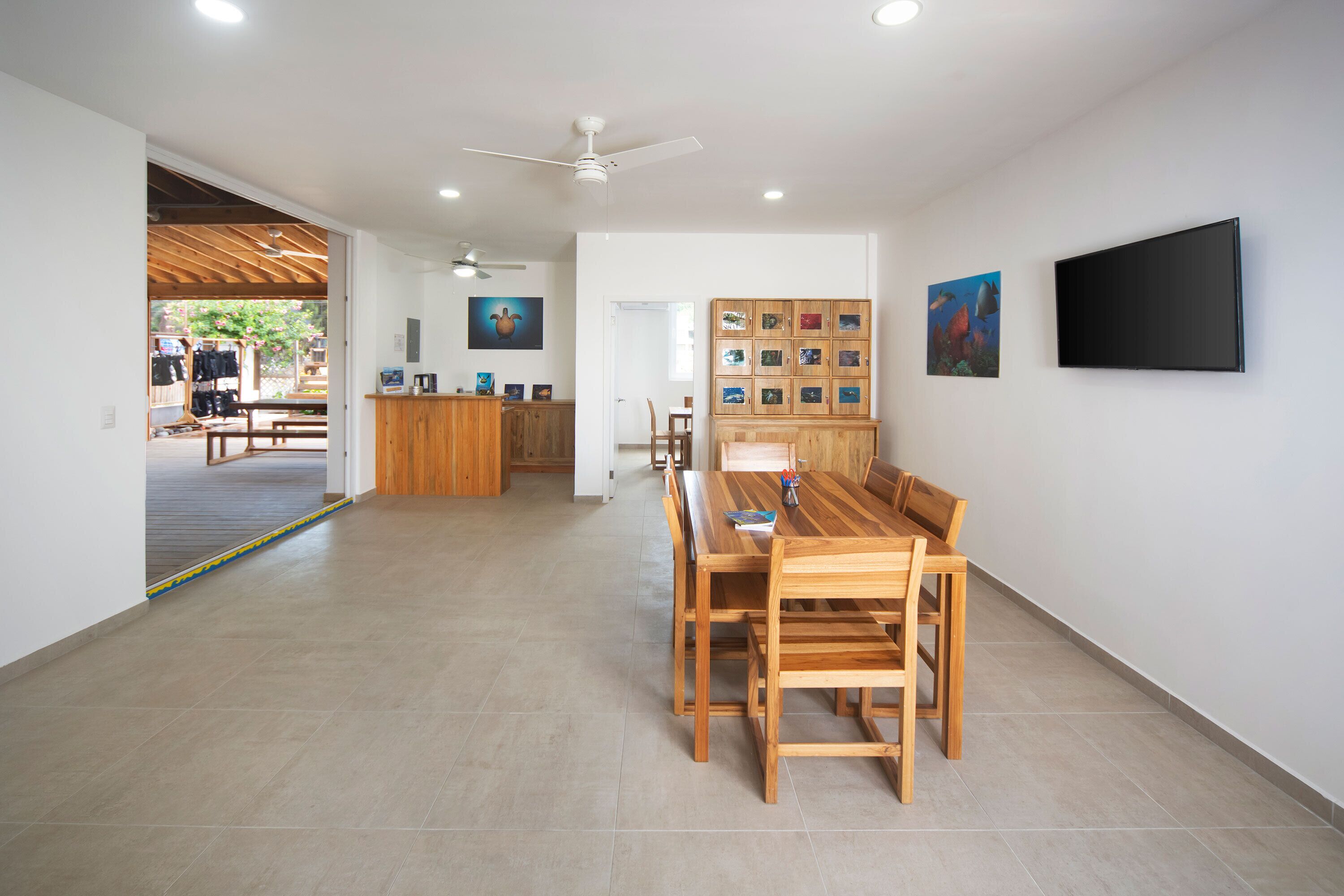 A spacious room with a wooden dining table and chairs, a ceiling fan, and a wall-mounted TV.