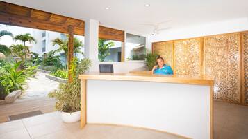 Un mostrador de recepción con encimera de madera, una planta en maceta y un panel decorativo en la pared.