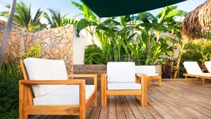 A wooden deck with four white cushioned chairs and a table, surrounded by lush tropical plants and a stone wall. - Naboo Resort & Dive Center - Adults Only (Roatan)