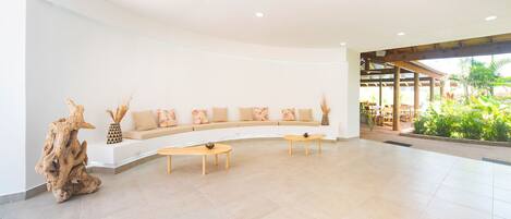 A spacious lobby with a curved seating area, two wooden tables, and a decorative tree sculpture.