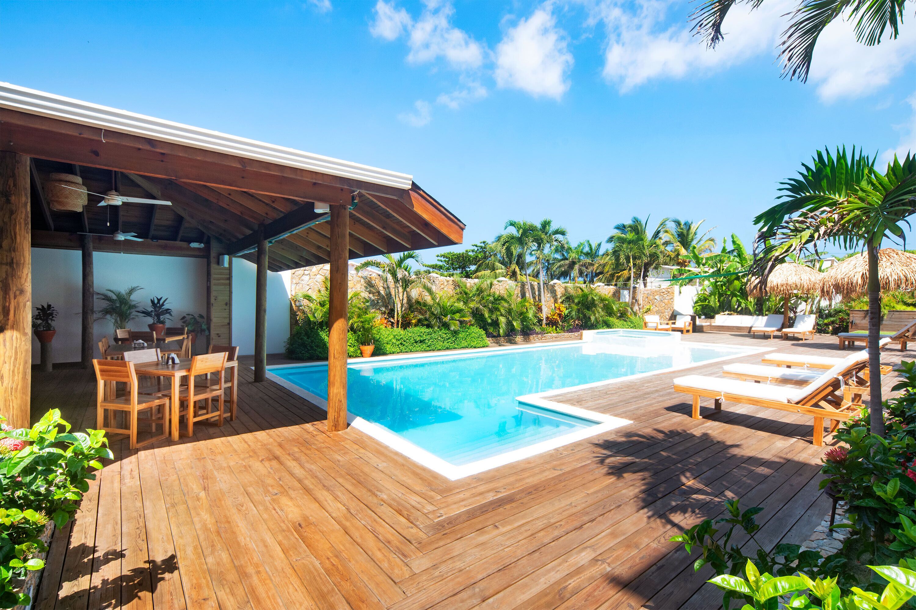 A wooden deck with a pool, lounge chairs, and a covered seating area.