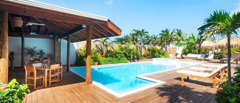 A wooden deck with a pool, lounge chairs, and a covered seating area.