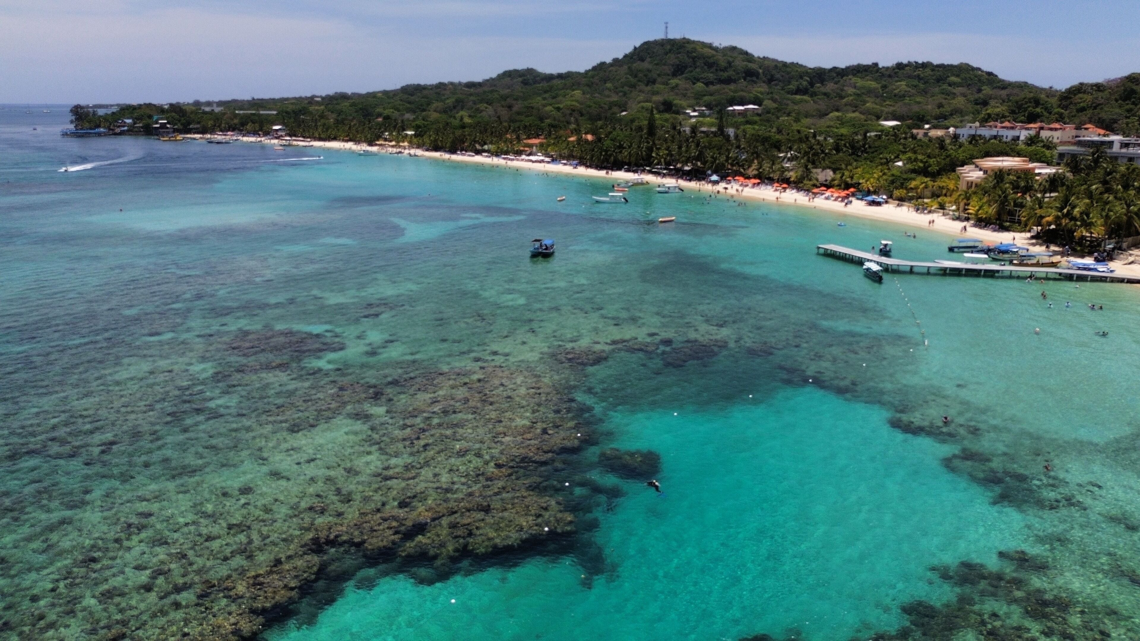 A coastal area with clear turquoise waters, a sandy beach, and a pier extending into the sea.