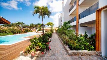 A pool area with a stone pathway, surrounded by lush greenery and a modern building with balconies.