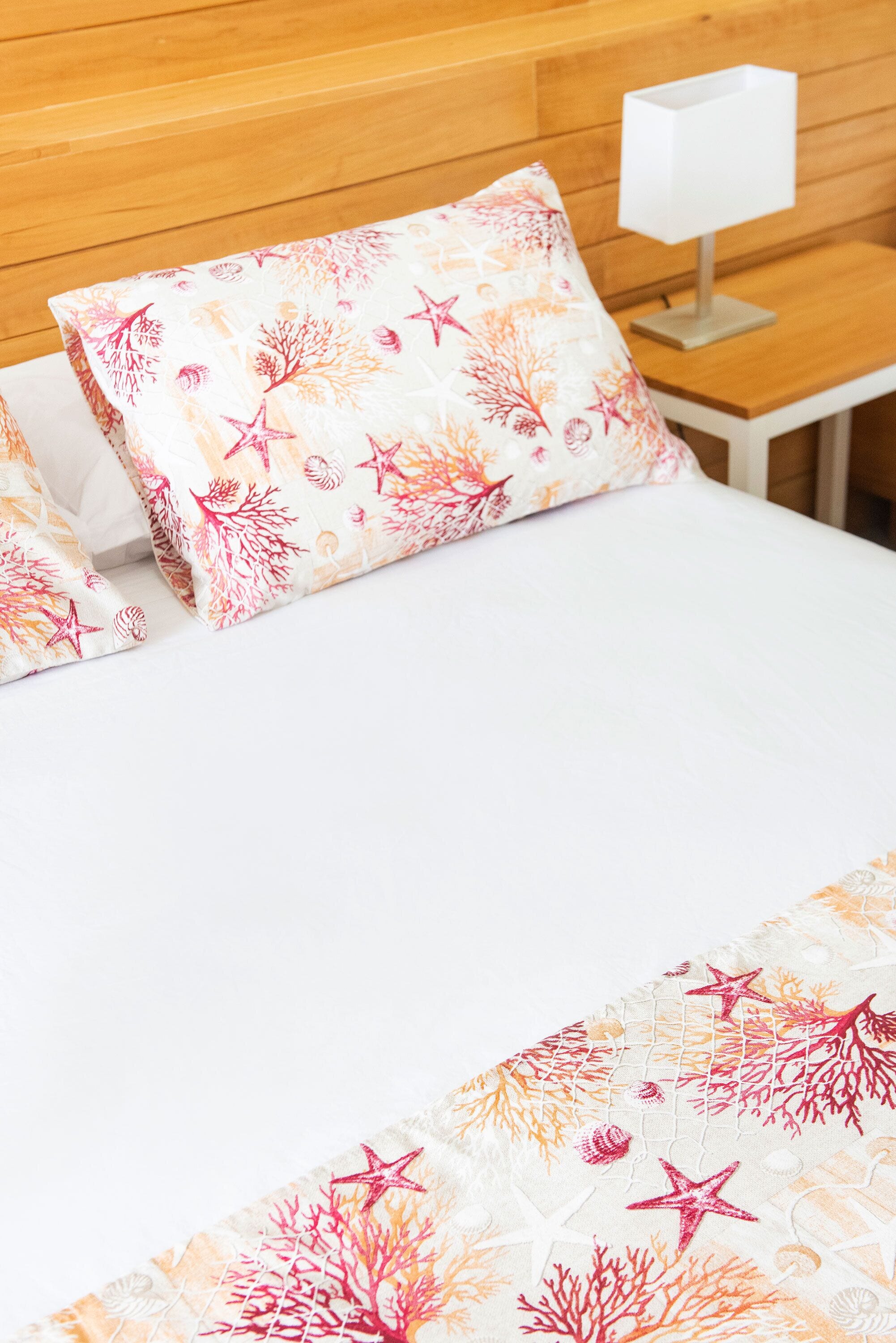 A bed with a white bedspread and pillows featuring a coral reef pattern.