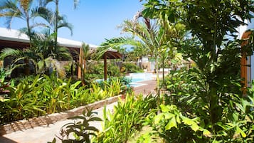 Un exuberante jardín con piscina, rodeado de diversas plantas tropicales y una pérgola.