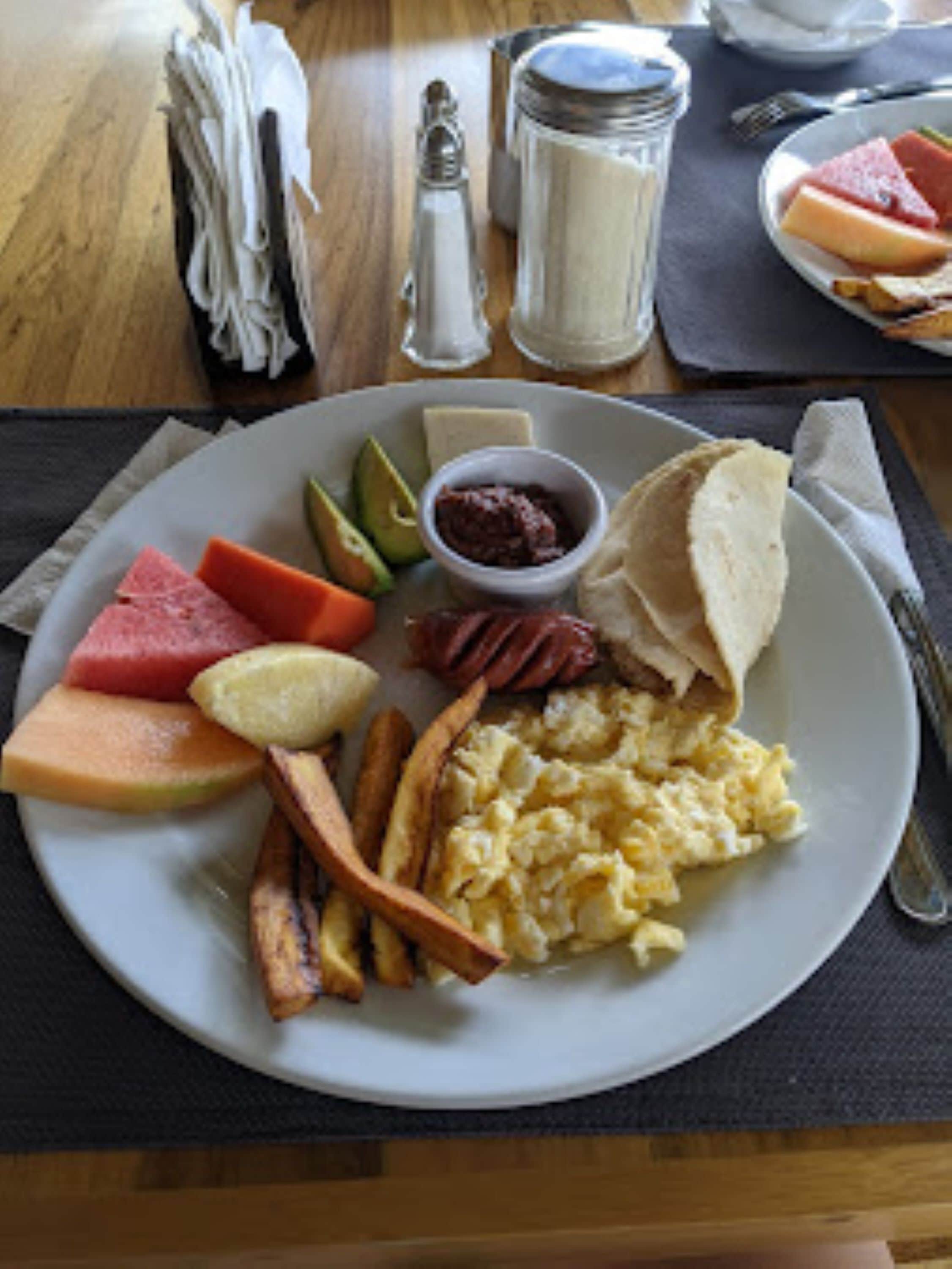 A breakfast plate with eggs, toast, fruit, and potatoes.