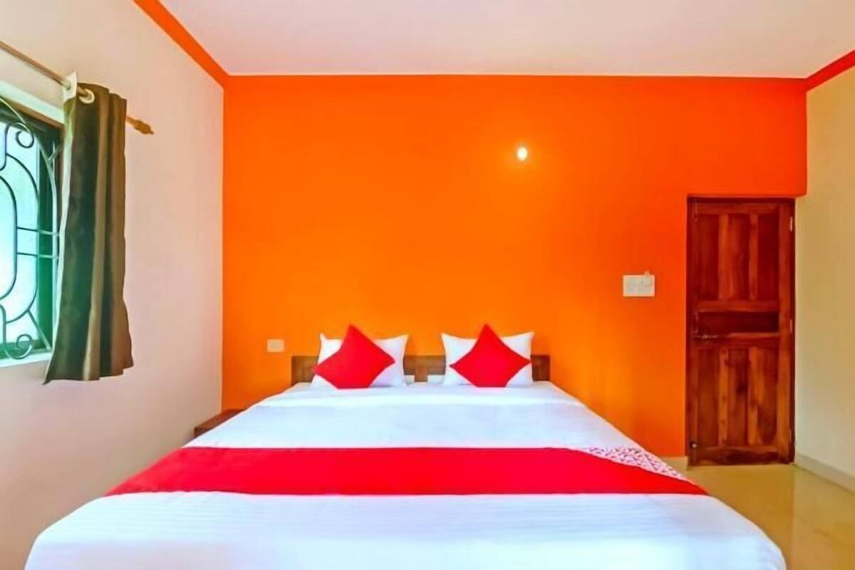 A hotel room with an orange wall, a bed with white and red bedding, and a wooden door.