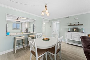 Une cuisine moderne avec des meubles blancs, une table à manger avec quatre chaises et un luminaire suspendu.