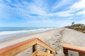 A beach with a wooden walkway leading to the shore, a clear sky, and the ocean.