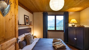 Quarto de madeira com uma cama, mesa de cabeceira, luminária e vista para montanhas pela janela.