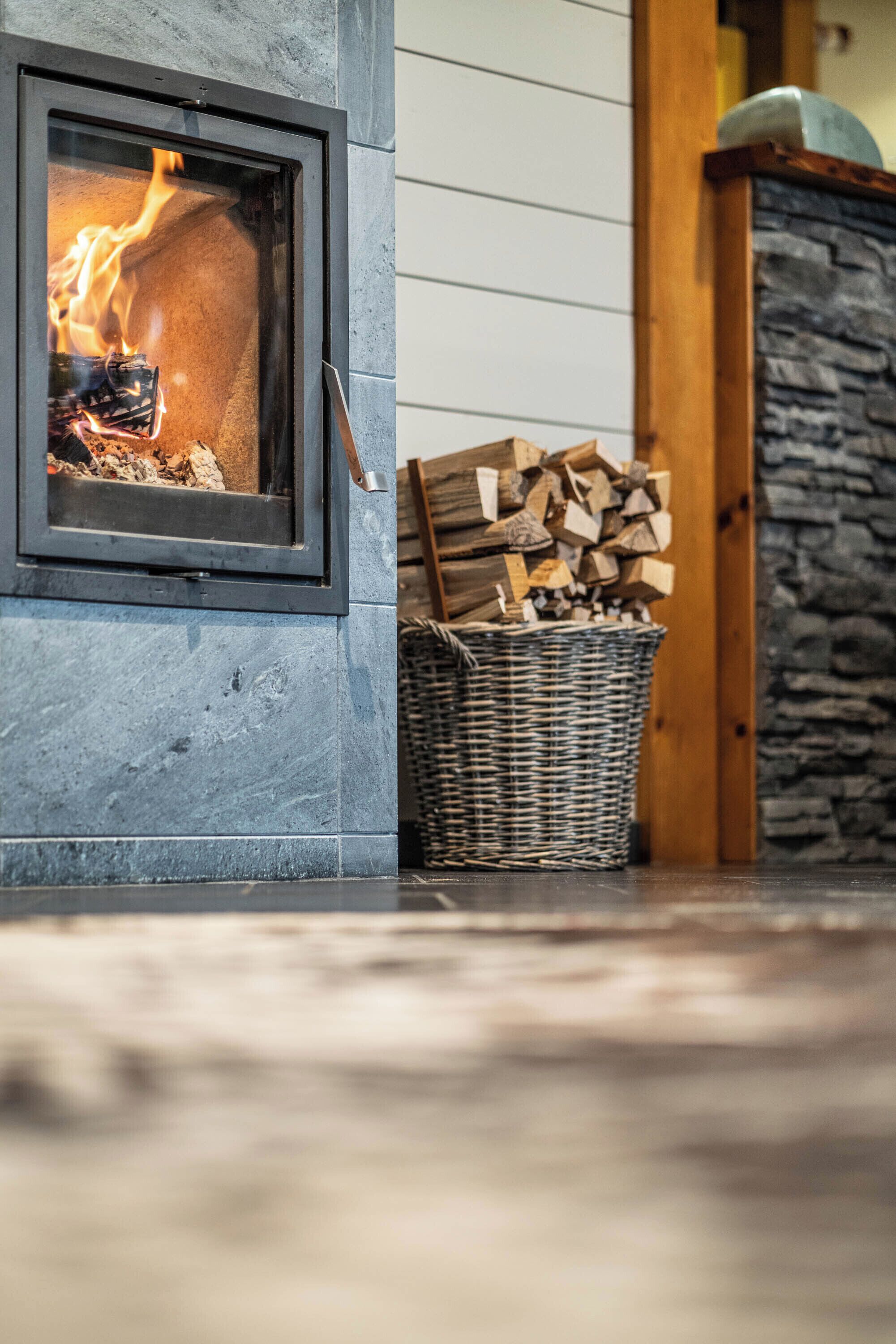 A stone fireplace with a glass door, a basket of firewood, and a stone wall.
