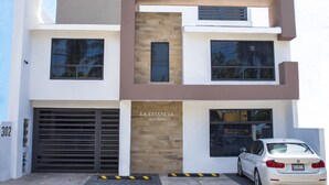 A modern multi-story building with a garage and a white car parked in front. - La Estancia Apartments Mazatlan 2 (Mazatlán)