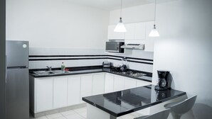 A modern kitchen with white cabinets, a black countertop, stainless steel appliances, and pendant lighting. - La Estancia Apartments Mazatlan 2 (Mazatlán)