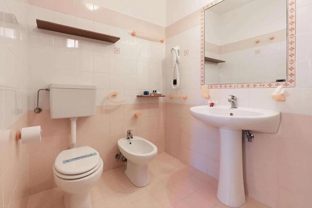 A bathroom with a toilet, bidet, sink, and mirror.
