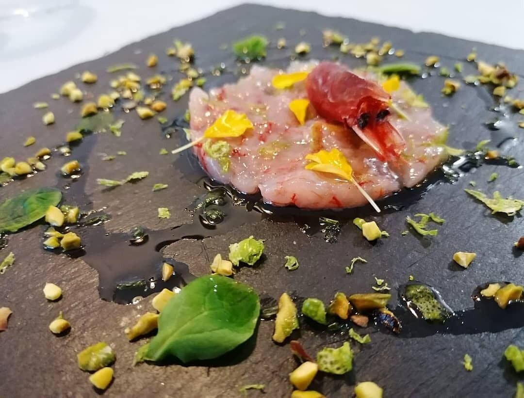 A dish with raw fish, garnishes, and a toothpick on a slate plate.