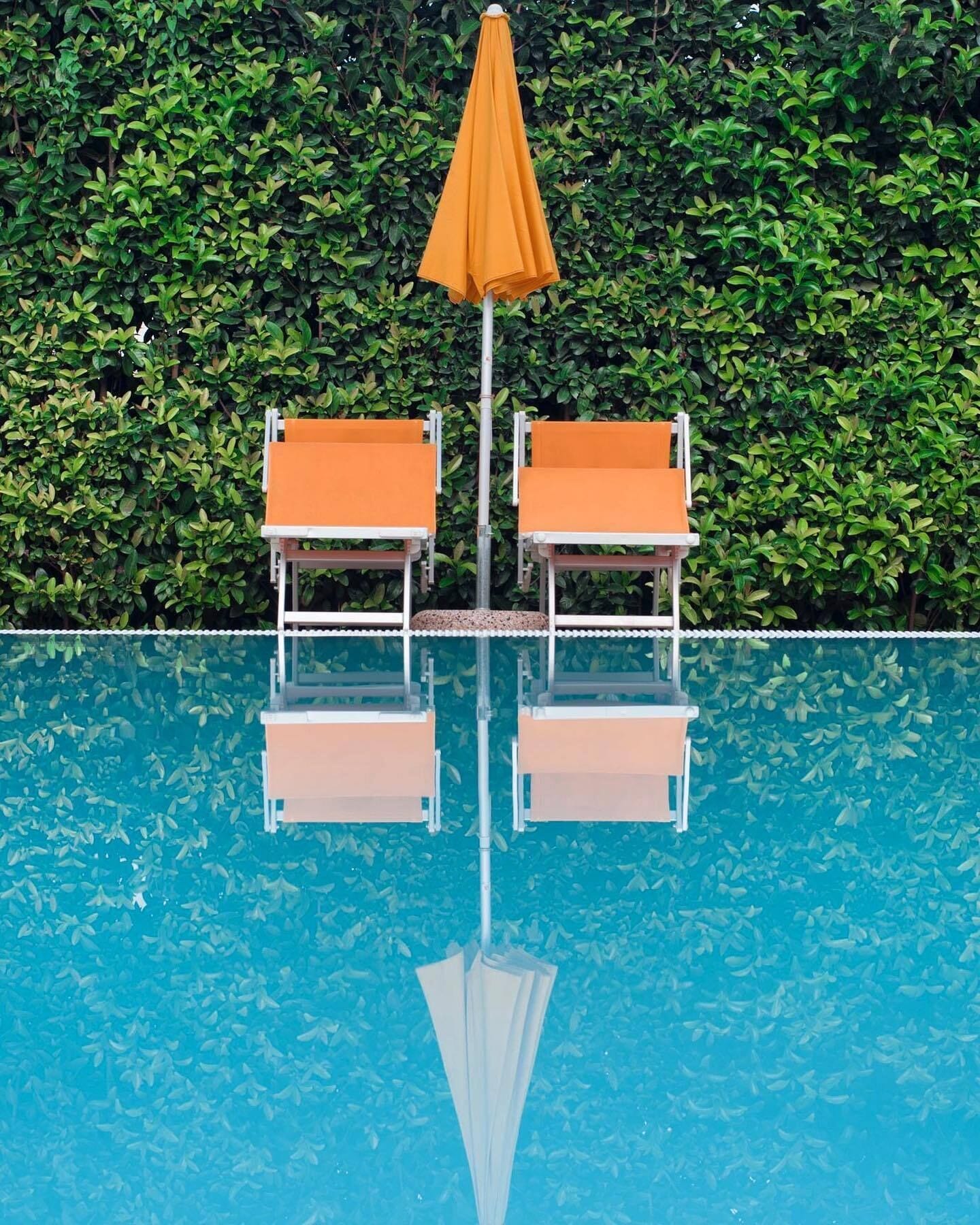 Una piscina con dos sillas de descanso y una sombrilla.