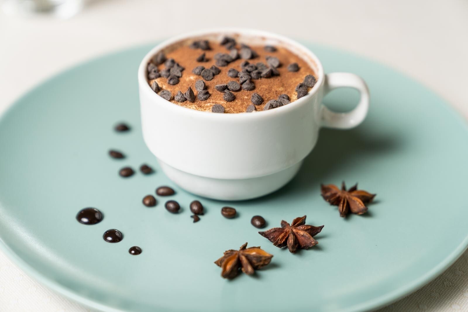 A cup of hot chocolate with chocolate chips and star anise on a light blue plate.