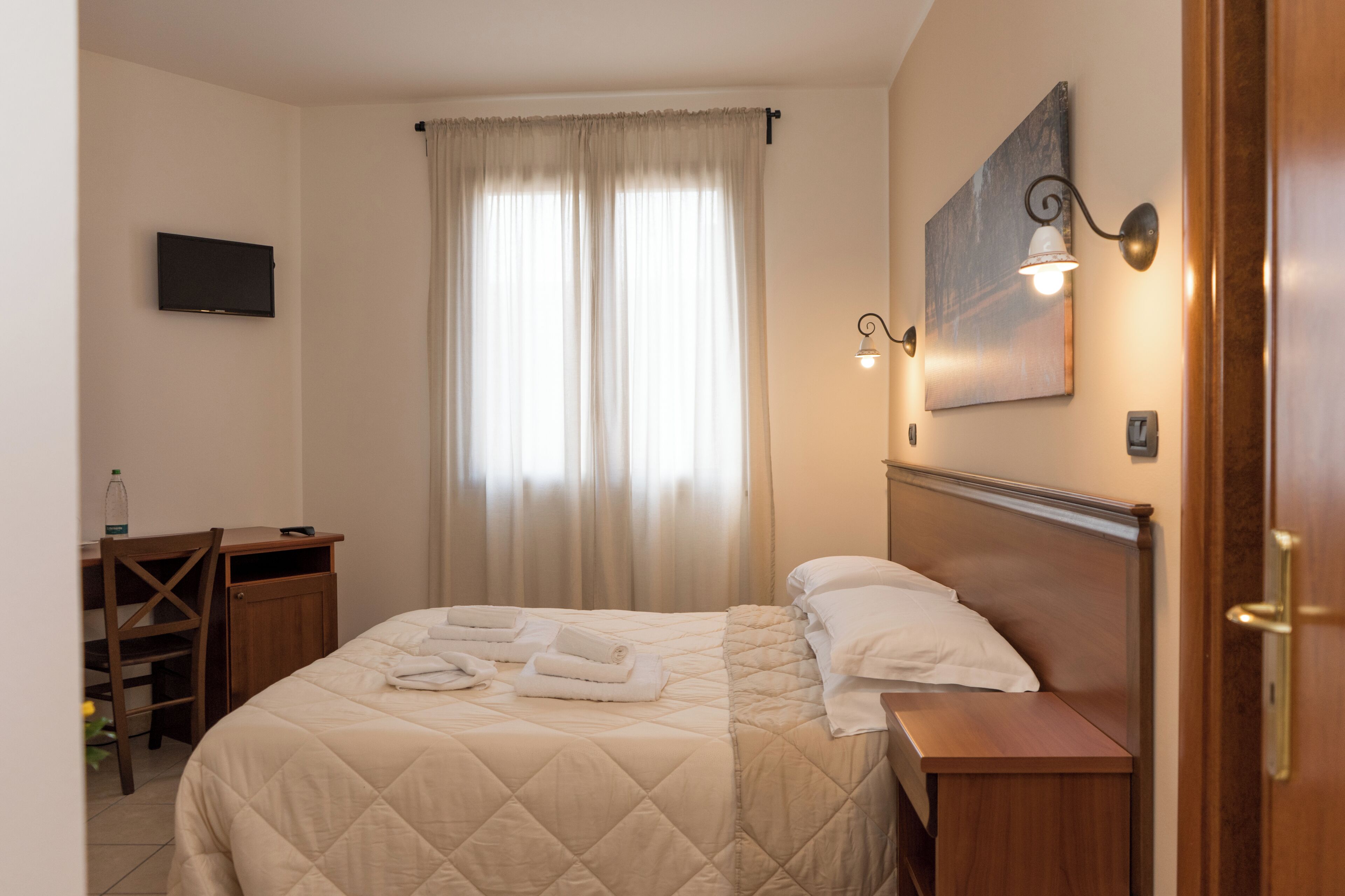 Une chambre d’hôtel bien rangée, avec un lit, un bureau, une chaise, une télévision et un tableau accroché au mur.