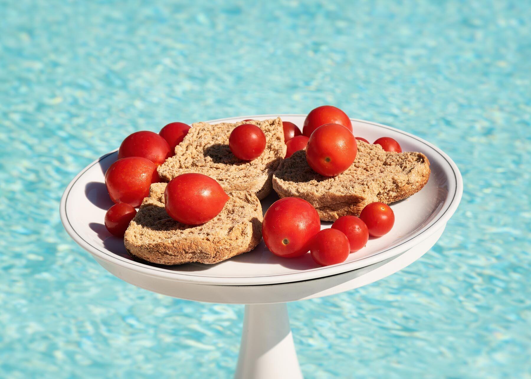 A white plate with slices of bread and cherry tomatoes on a white pedestal table.
