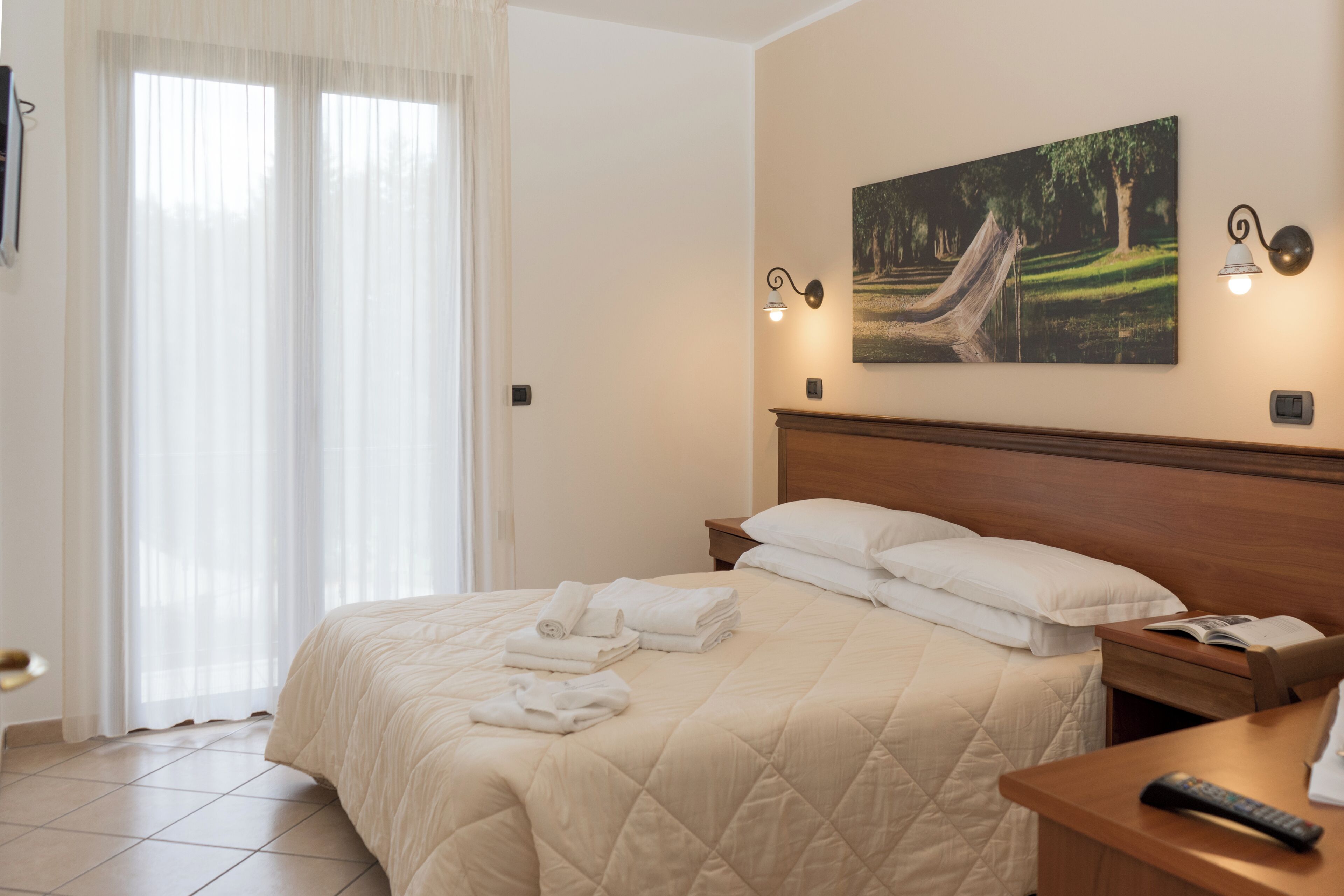 Une chambre d’hôtel avec un lit, une table de chevet, un tableau et une fenêtre avec des rideaux.