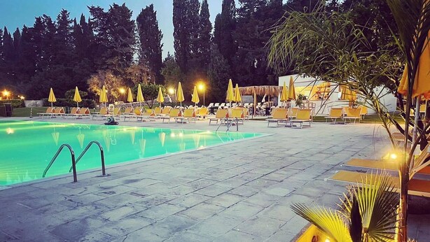 Una piscina con sillas de descanso y sombrillas, rodeada de árboles.