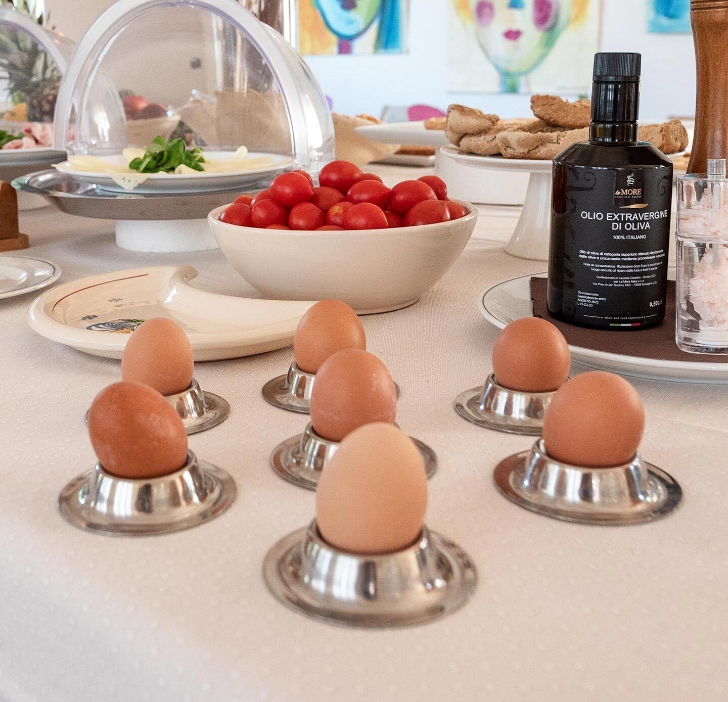 Un buffet della colazione con diversi cibi, tra cui una ciotola di pomodori rossi, una bottiglia d'olio d'oliva e diverse uova su un vassoio.