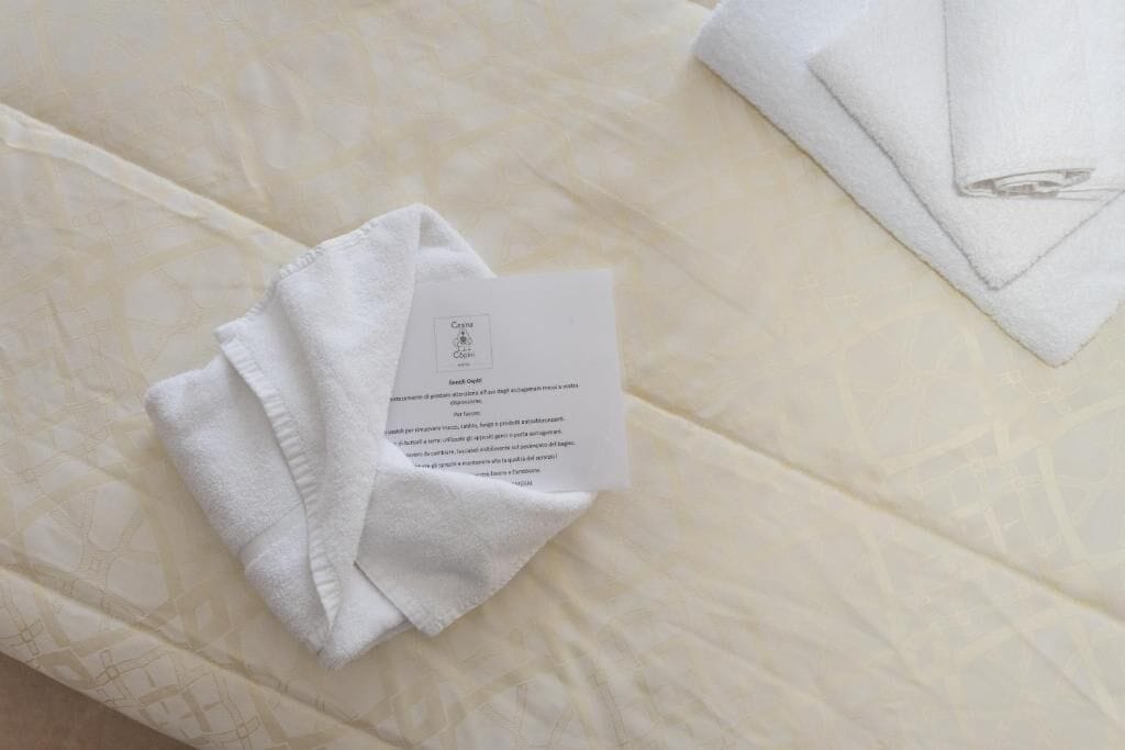 A neatly folded white towel and a card on a bed with a patterned bedspread.