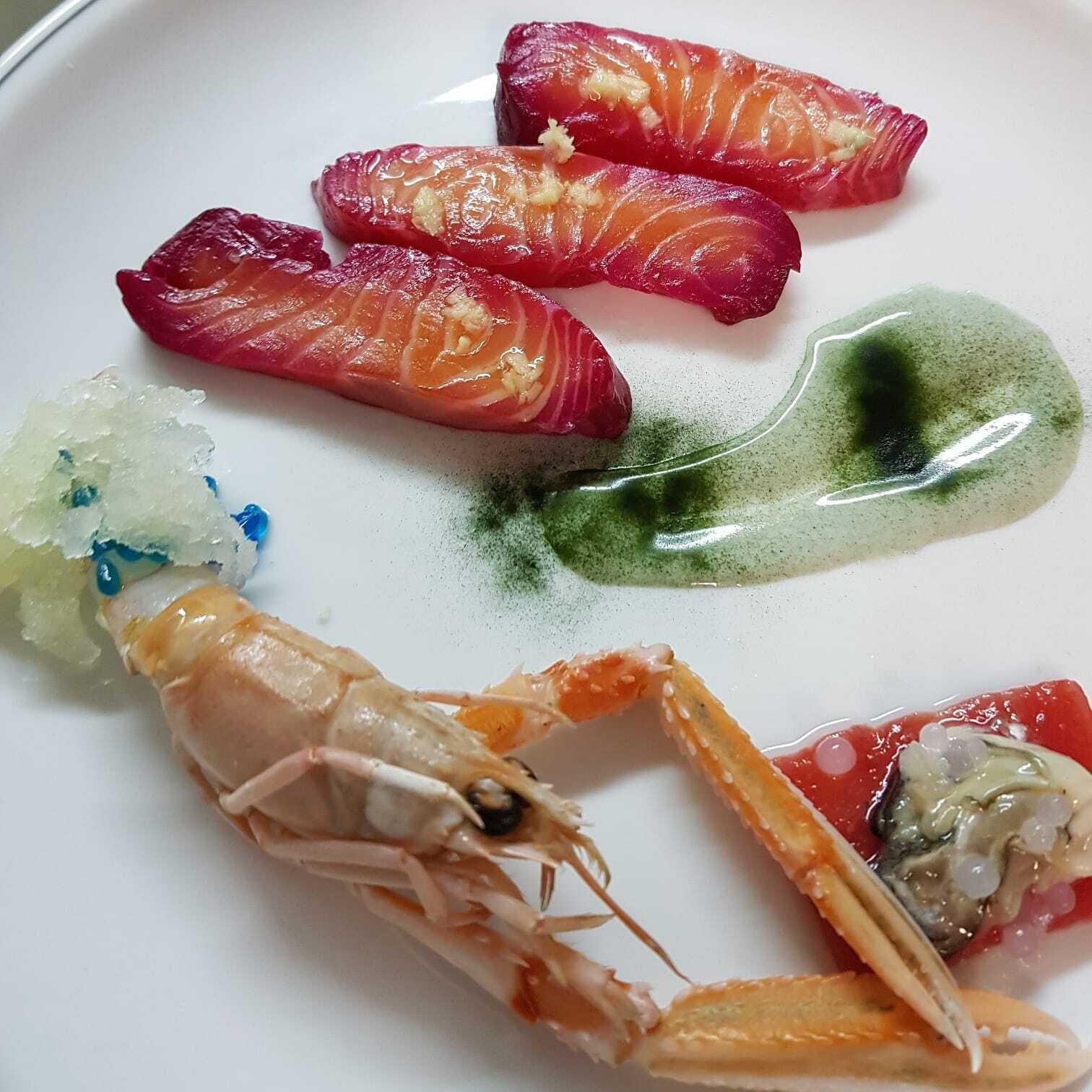A plate with sashimi, a shrimp, and green sauce.