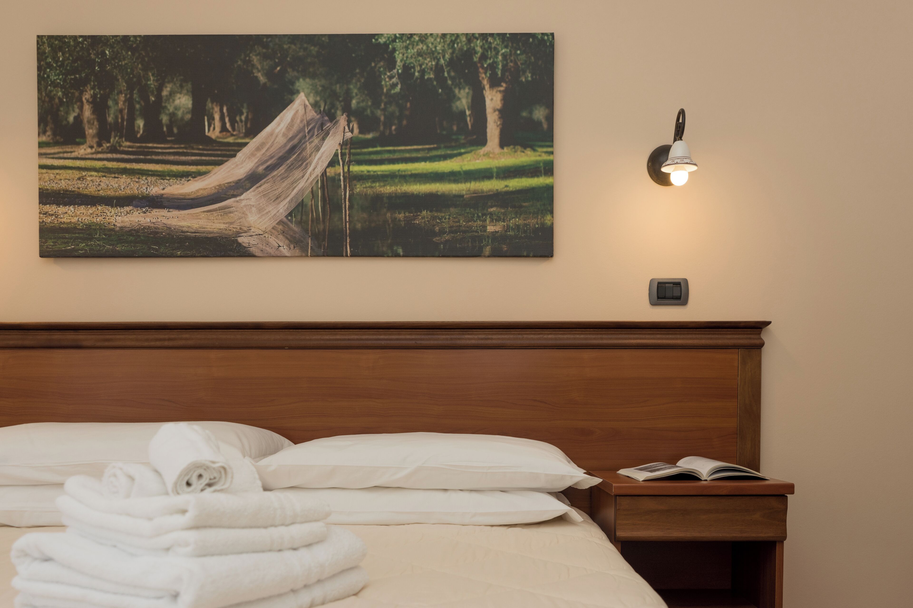 Un lit bien fait, avec du linge de lit blanc, un hamac et un luminaire fixé au mur.