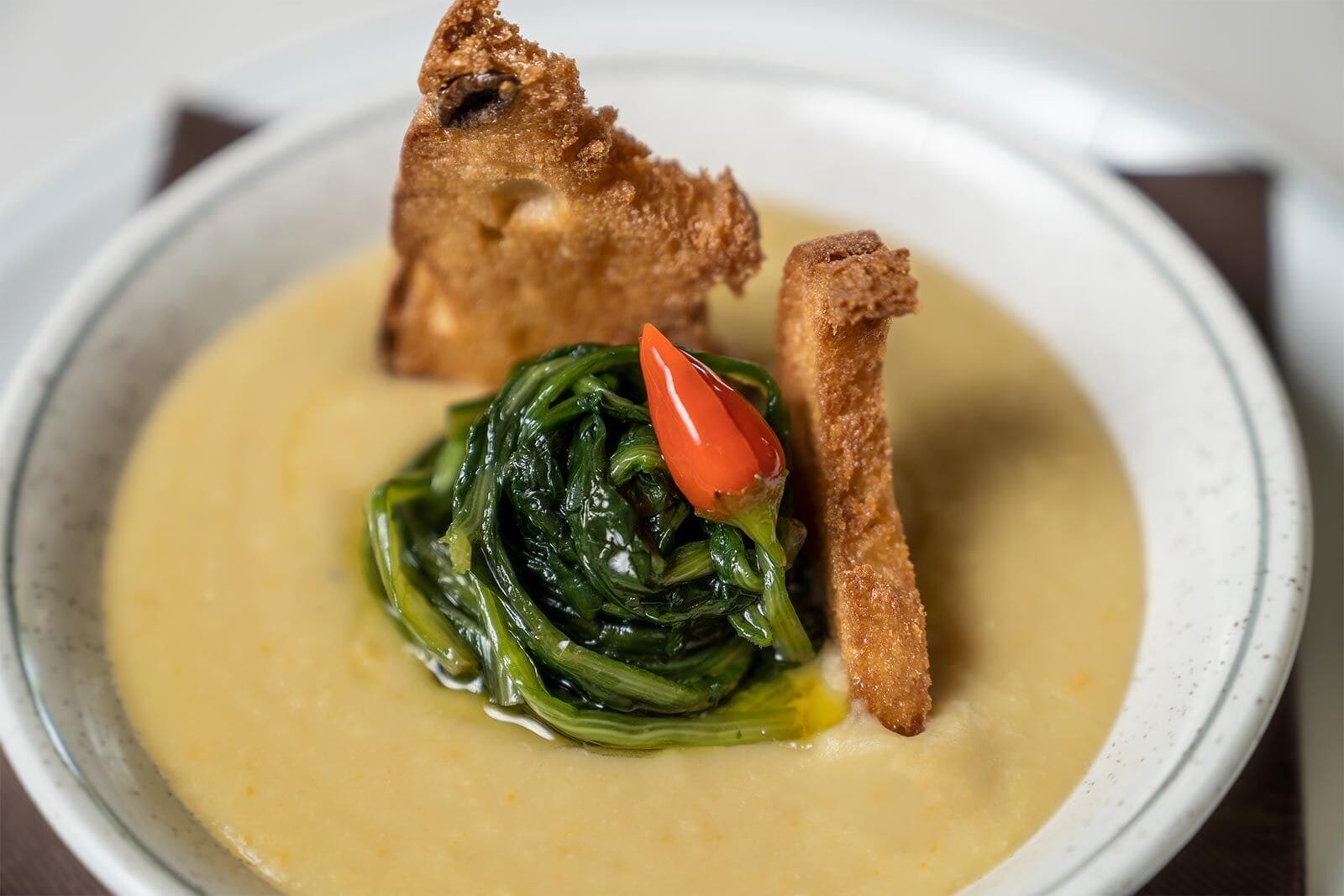 A bowl of soup with a side of greens and two pieces of bread.
