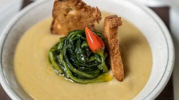 A bowl of soup with a side of greens and two pieces of bread.