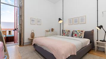 Un dormitorio con cama, lámparas de noche, cómoda y cuadros en la pared.