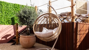 Une chaise suspendue en osier, dotée d’un coussin, une plante en pot et une clôture en bois dans une cour.