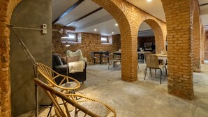 Un intérieur spacieux agrémenté d’arches en briques, un coin salon confortable avec un canapé et des fauteuils, une table à manger, et une cuisine ouverte visible au fond.