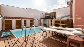 Une terrasse en bois avec une piscine, des chaises longues et une petite table.