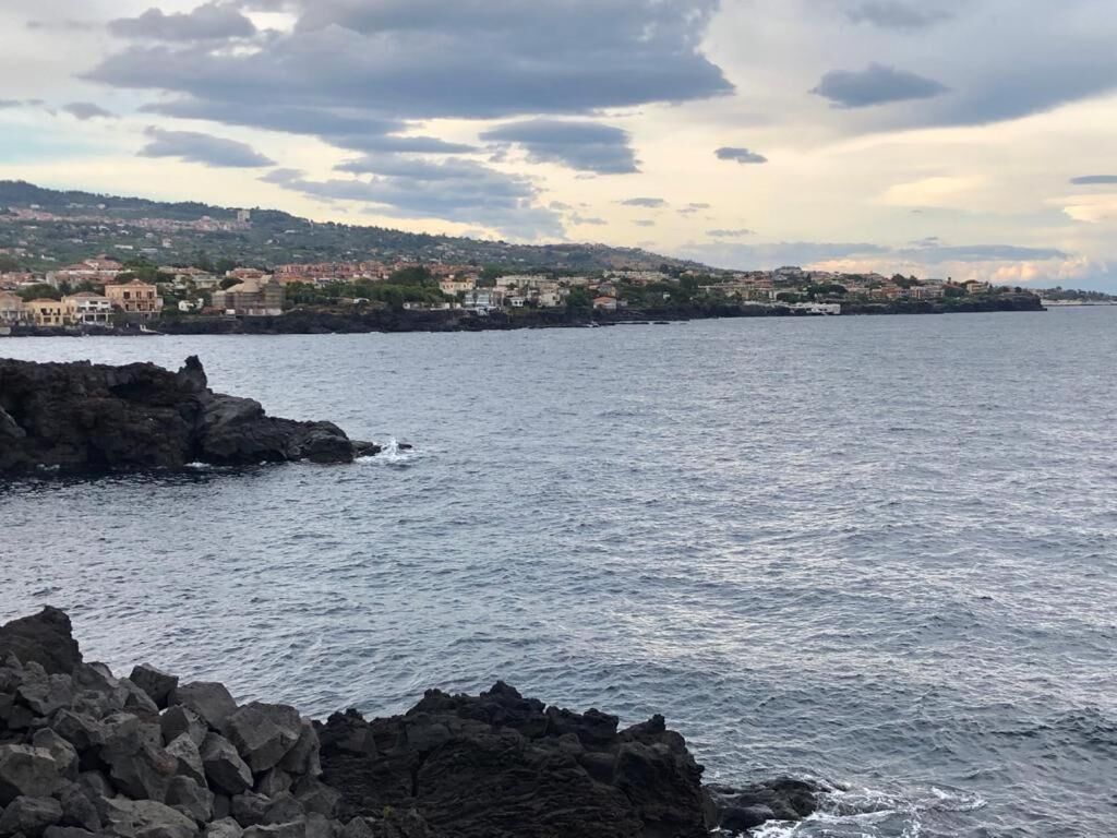 A coastal view with rocky shoreline, calm sea, and distant buildings on a hilly landscape.