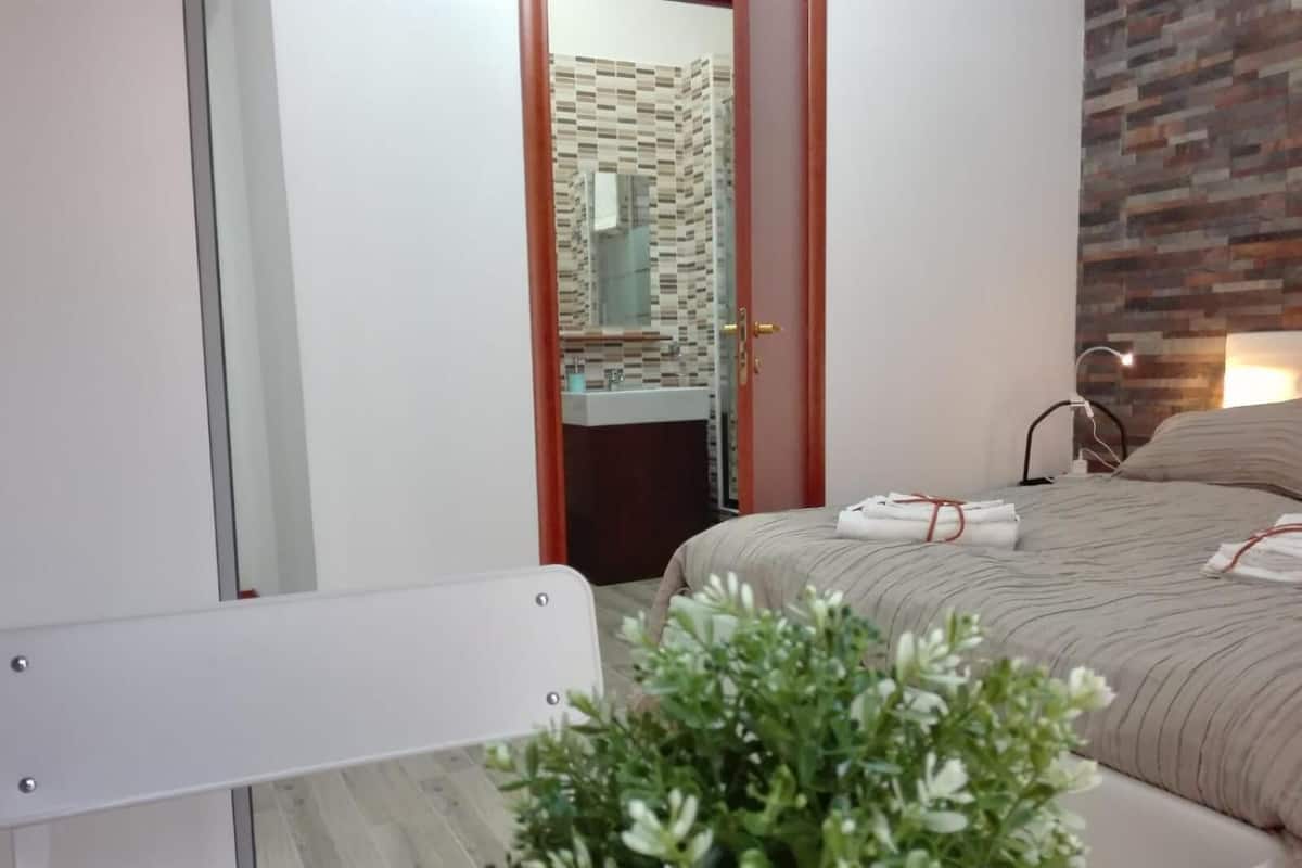 Ein modernes Schlafzimmer mit Bett, Nachttisch, Spiegel und Blick ins Badezimmer.