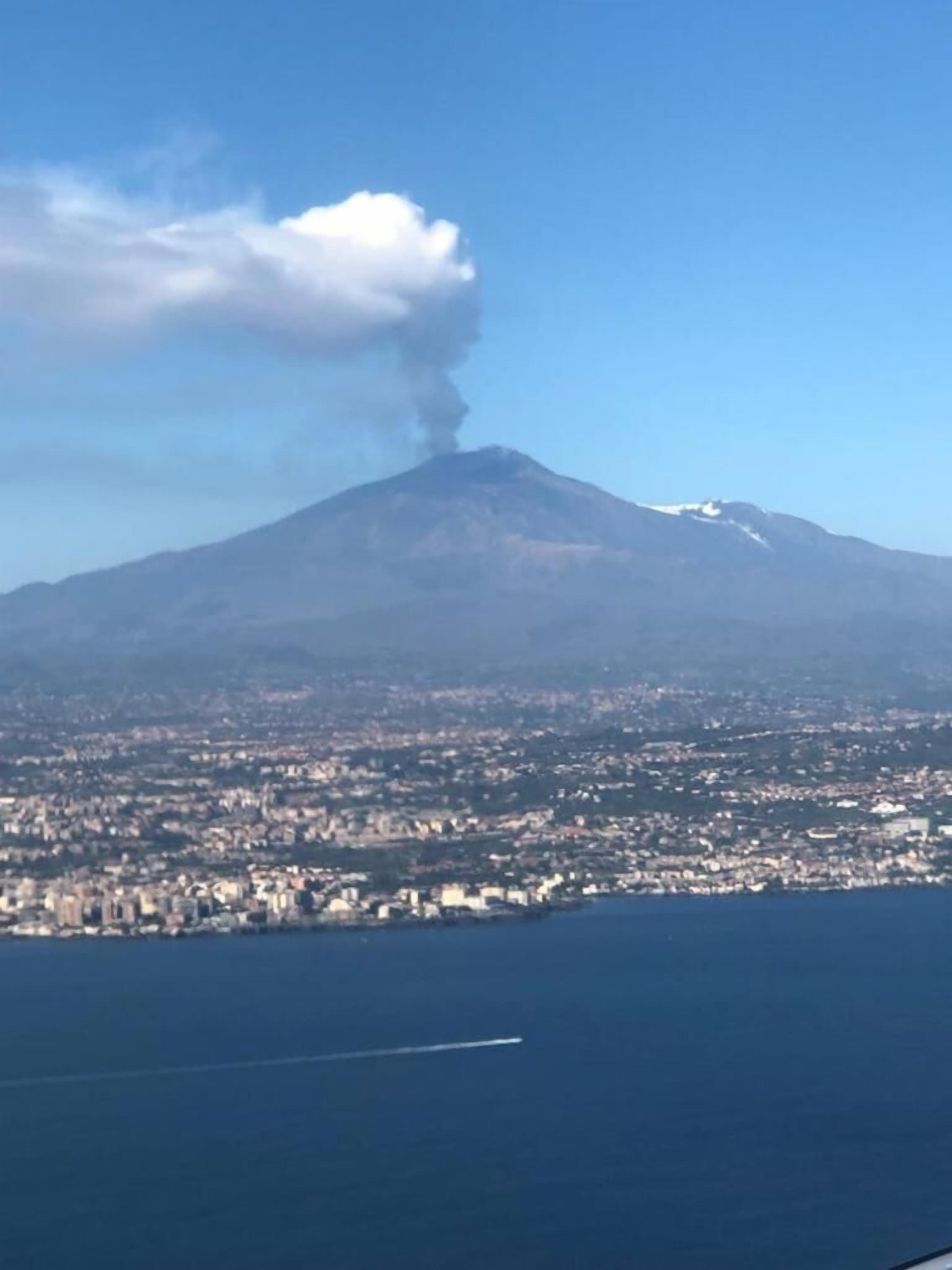 Un volcán con humo, un paisaje urbano y una masa de agua.