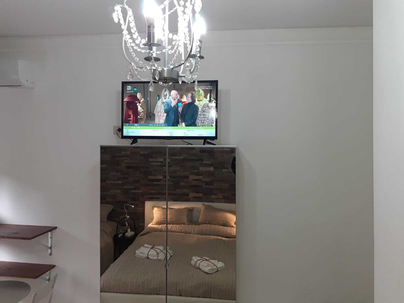 Una habitación de hotel con cama, televisor montado encima y una araña.