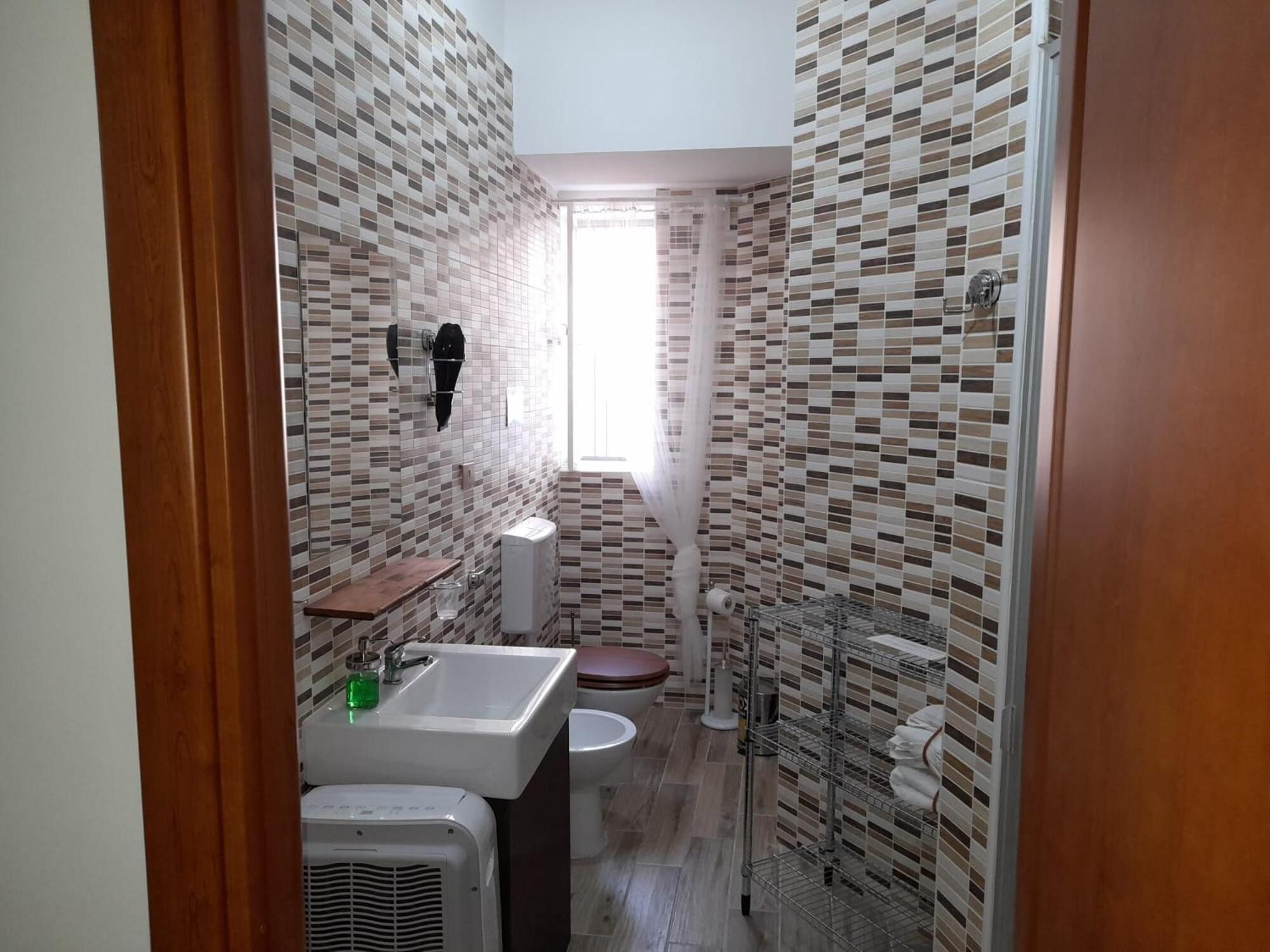 Un baño pequeño con pared de azulejos, un lavabo, un inodoro y una zona de ducha.