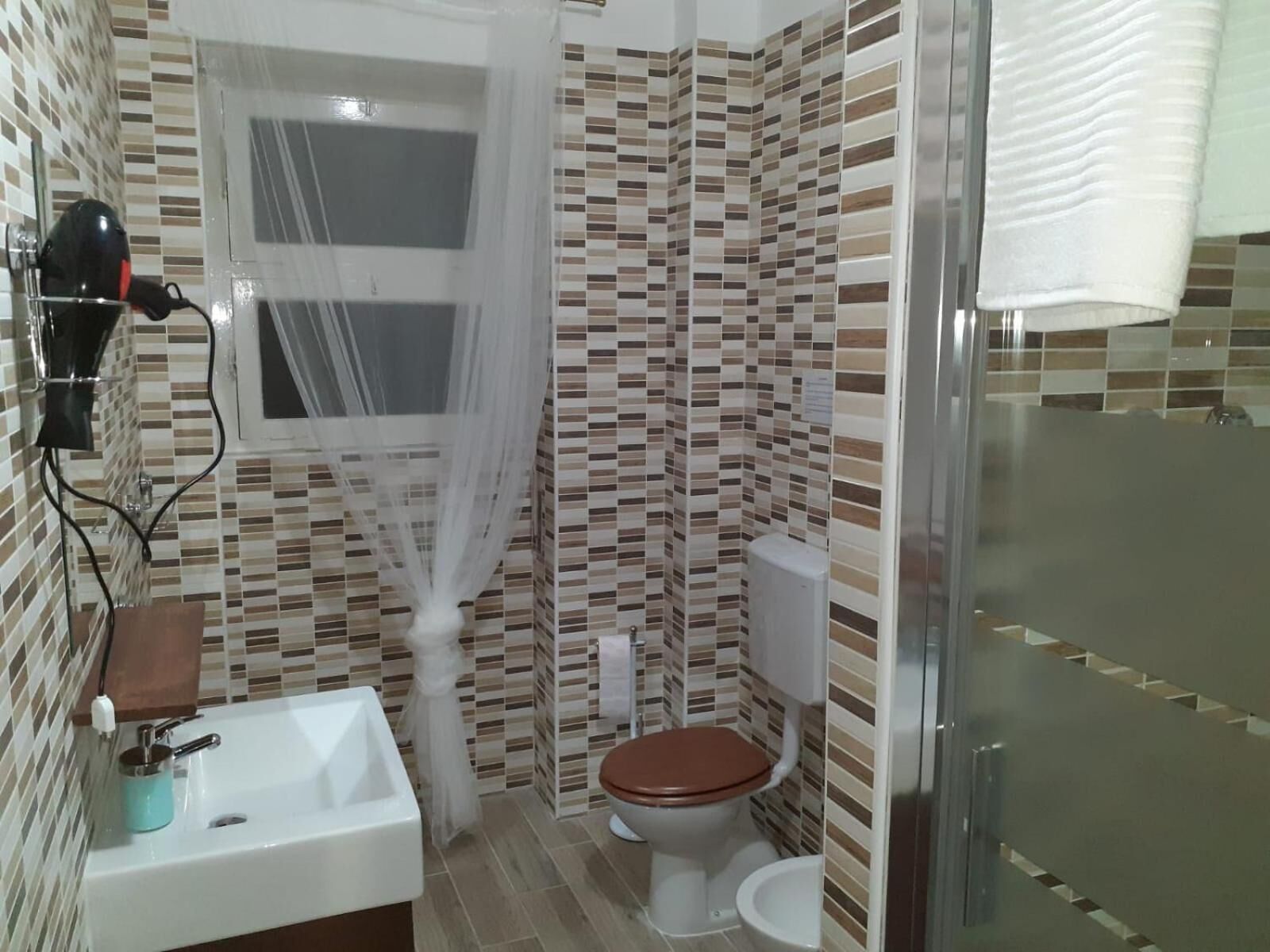 Un baño con salpicadero de azulejos, un lavamanos blanco con dispensador de jabón, un inodoro y una zona de ducha.